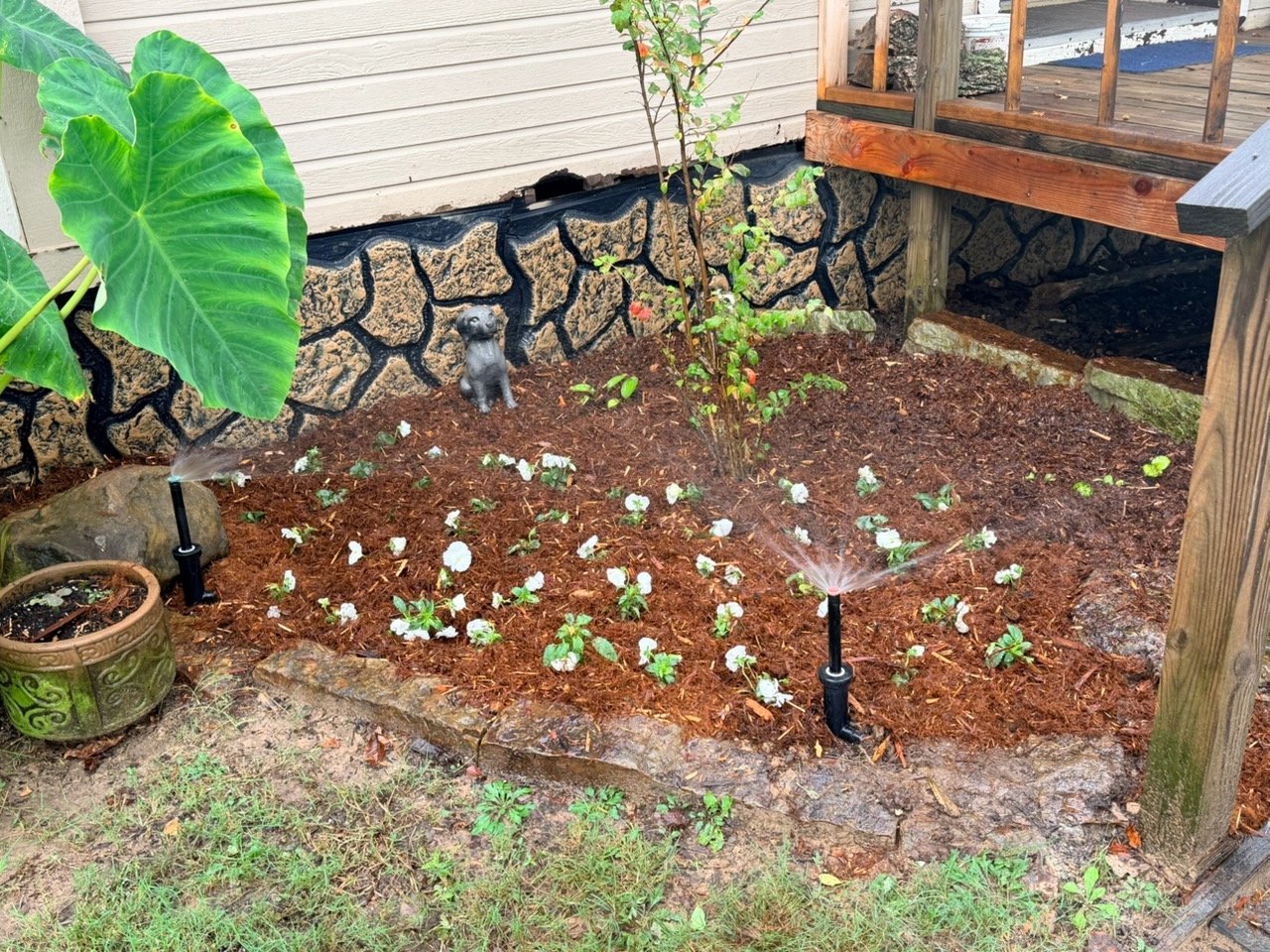 Fresh mulched flowerbed with white flowers and two sprinkler heads spraying